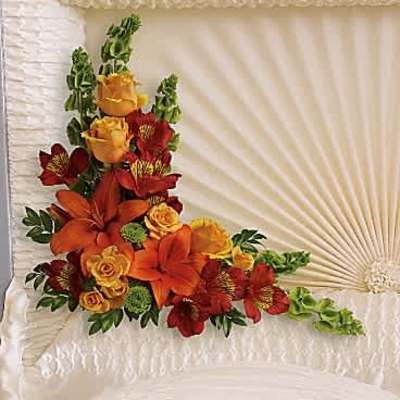 Corner casket spray with orange lilies, yellow roses and red flowers inside a cream casket.