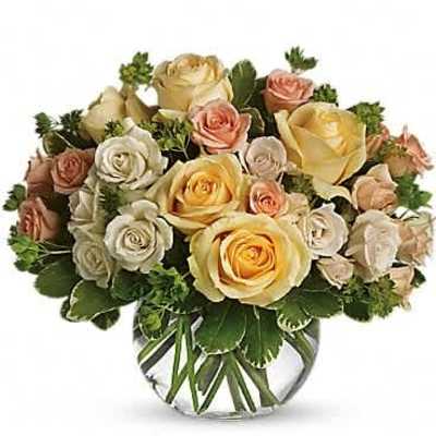 Round arrangement of yellow, cream, and peach roses in a clear glass bowl vase