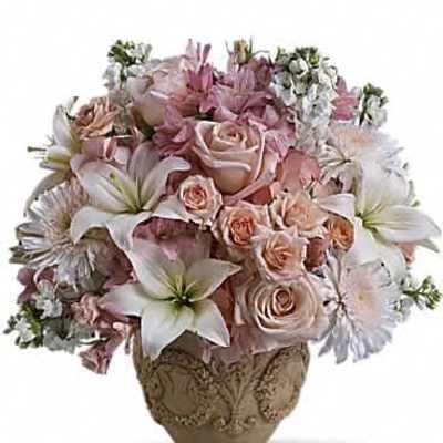 Round arrangement of blush roses, white lilies, and soft pink blooms in an ornate beige ceramic vase