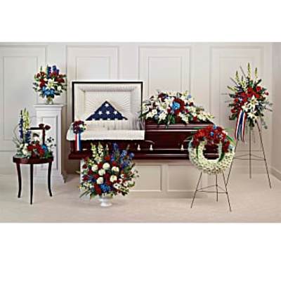 Patriotic red, white, and blue funeral floral set with casket spray, wreath, and standing sprays around a casket.
