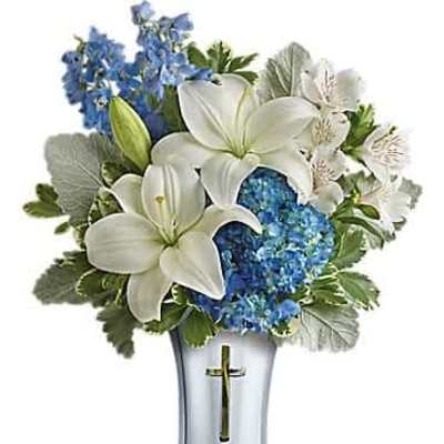 White lilies and blue hydrangeas in a silver vase with a gold cross emblem