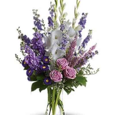 Tall arrangement of purple blooms, white flowers, and pink roses in a clear glass vase