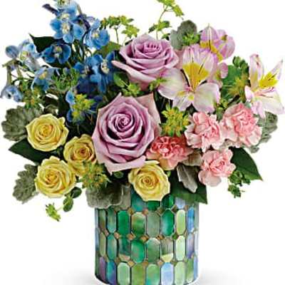 Mixed bouquet of pastel roses, lilies, carnations, and blue flowers in a mosaic cylinder vase