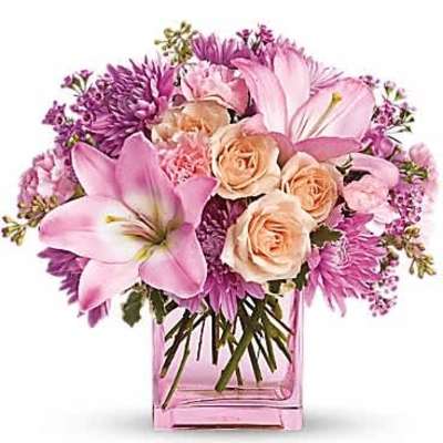 Pink and peach flower arrangement with lilies and roses in a pink glass cube vase