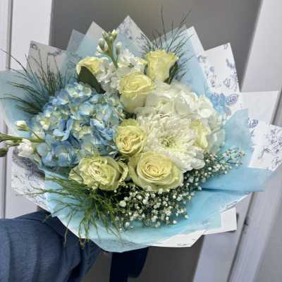 Bouquet of pale yellow roses, blue hydrangeas, and white flowers wrapped in blue paper
