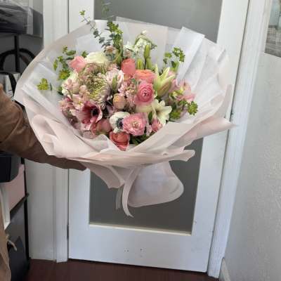 Hand-tied bouquet of pink and white mixed flowers wrapped in pale paper