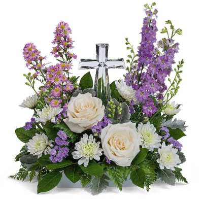 White roses and purple flowers arranged around a clear glass cross