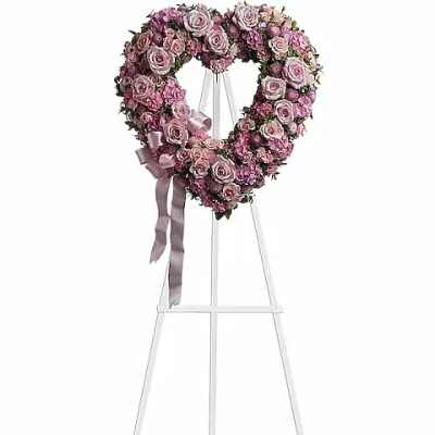 Heart-shaped pink rose wreath on a white stand with ribbon