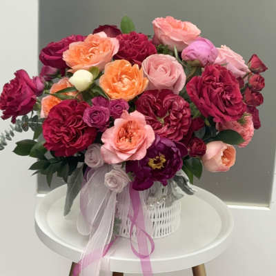 Bouquet of pink, peach, and magenta roses in a white basket with ribbon