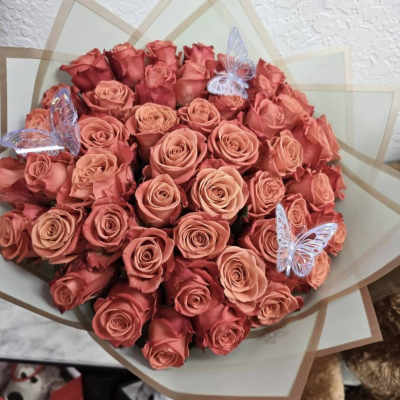Bouquet of coral and pink roses wrapped in translucent paper with butterfly picks