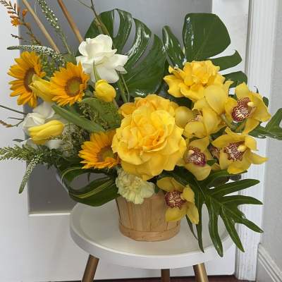 Yellow floral arrangement in a wooden basket with orchids and sunflowers