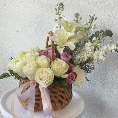Basket arrangement of cream lilies, roses, and pink blooms with ribbon