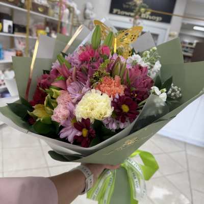 Mixed bouquet of pink, white, and yellow flowers wrapped in green paper