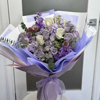 Lavender and white rose bouquet wrapped in purple paper with a ribbon