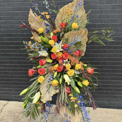 Tall floral standing spray with red, yellow, and white blooms on a display easel