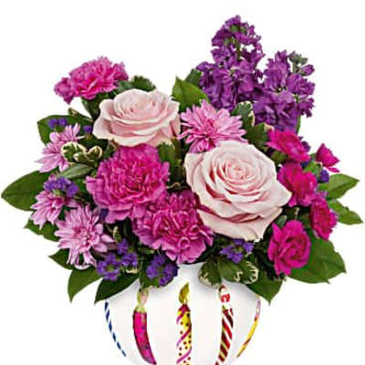 Low pink and purple mixed flower arrangement in a white bowl vase with painted birthday candles