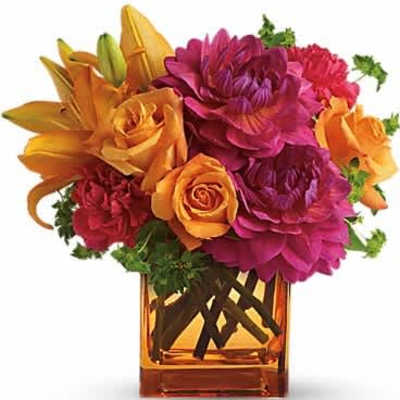 Square orange vase of orange lilies and roses with bright pink dahlias and red carnations.