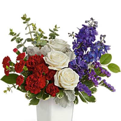 Red carnations, white roses, and blue flowers in a white square vase