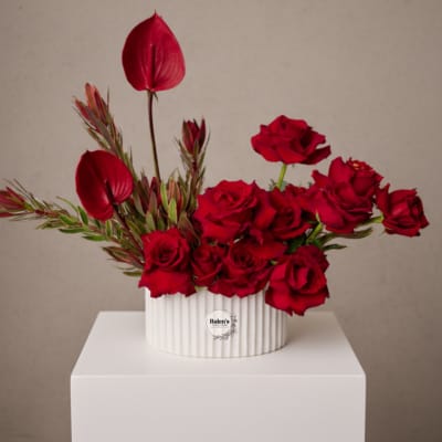 Red roses and burgundy tropical blooms in a white ribbed vase