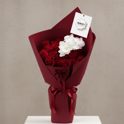 Bouquet of red roses with white orchids wrapped in burgundy paper