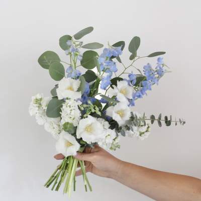 Handheld bouquet of white and blue flowers with round eucalyptus leaves