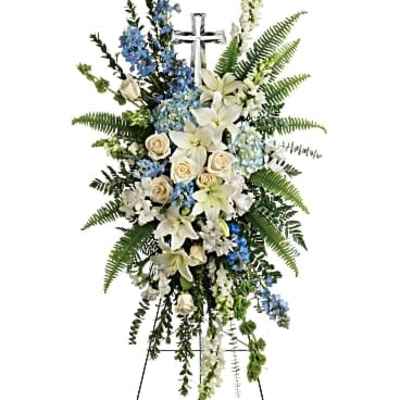 Tall white and blue standing floral spray with lilies and roses on an easel with a silver cross