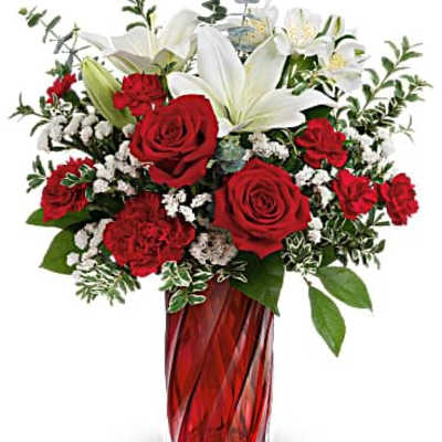 Red and white flower arrangement with roses, carnations, and lilies in a tall red glass vase