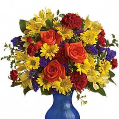 Bright bouquet of orange roses, red carnations and yellow daisies in a cobalt blue glass vase