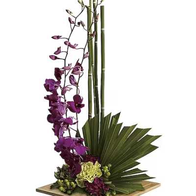Tall floral arrangement with purple orchids and green tropical leaves in a wooden base