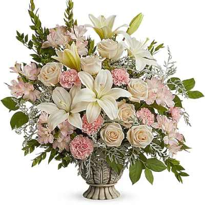 White lilies and cream roses in a decorative vase with pink filler flowers