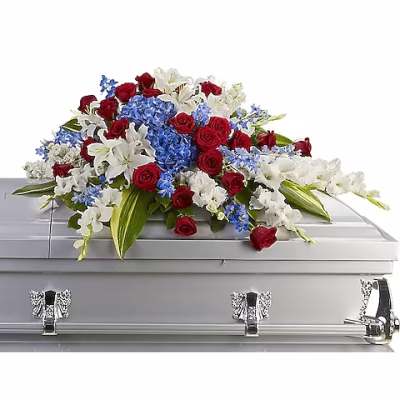 Red roses, white lilies, and blue flowers arranged on a silver casket