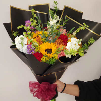 Mixed bouquet with a sunflower, roses, and white blooms wrapped in black paper