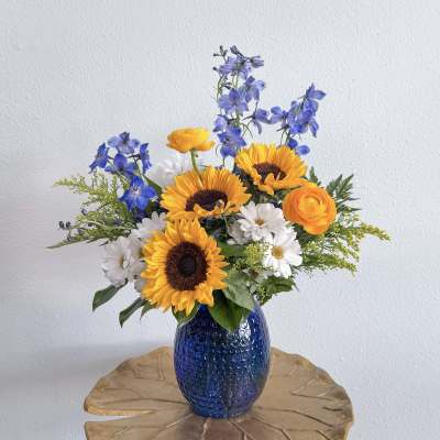 Bouquet of sunflowers, blue delphinium, and white daisies in a blue vase