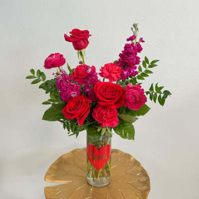 Red and pink flower arrangement in a glass vase with a heart label