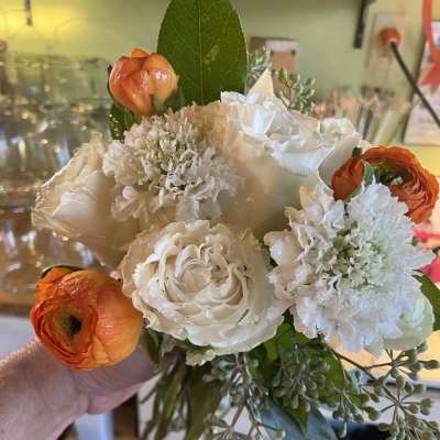 Handheld bouquet of white roses, white blooms, and orange ranunculus