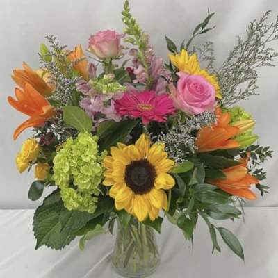 Mixed bouquet with sunflowers, pink roses, orange lilies, and a glass vase