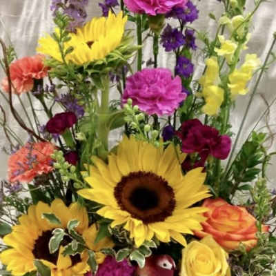 Tall mixed flower arrangement with sunflowers, roses, and purple blooms in a basket