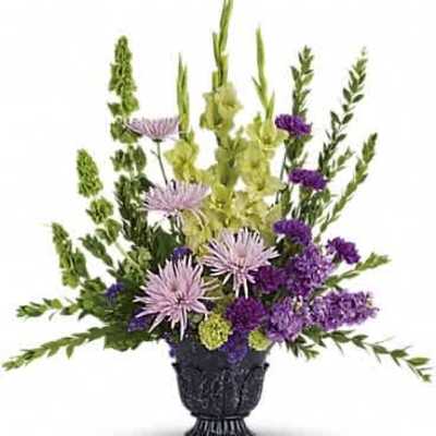 Tall arrangement of green bells of Ireland, lavender mums, and purple flowers in a dark urn vase