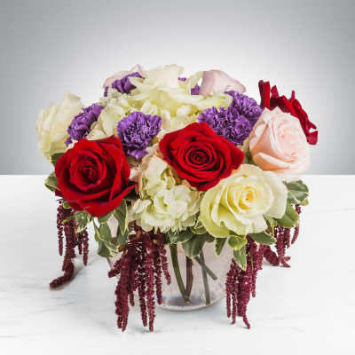 Mixed bouquet of roses, carnations, and hydrangeas in a clear glass vase