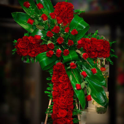 Large cross-shaped arrangement of red roses with glossy green leaves