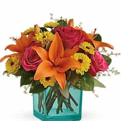 Bright mix of orange lilies, pink roses, and yellow blooms in a teal glass cube vase