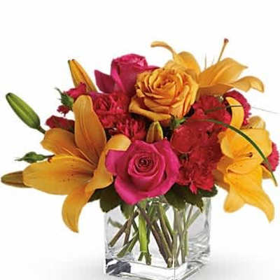 Compact arrangement of orange lilies and hot pink roses in a clear glass cube vase