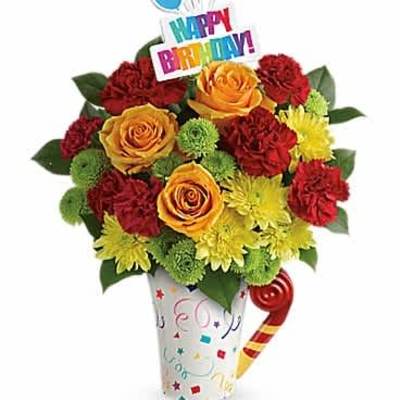 Birthday mug arrangement with yellow mums, red carnations, and orange roses with a Happy Birthday pick