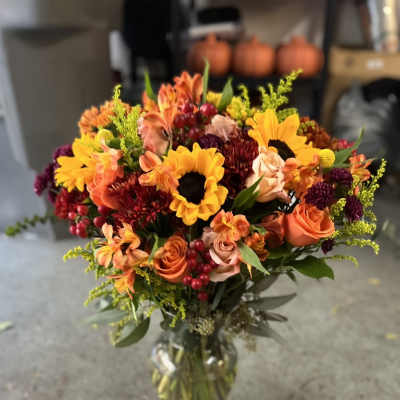 Mixed bouquet of sunflowers, roses, and orange blooms in a glass vase