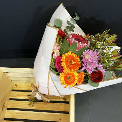Mixed bouquet with orange daisies, pink roses, and purple blooms in white wrap