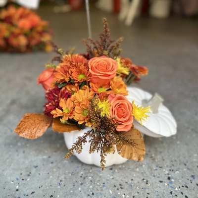 Orange and yellow floral arrangement in a white pumpkin container