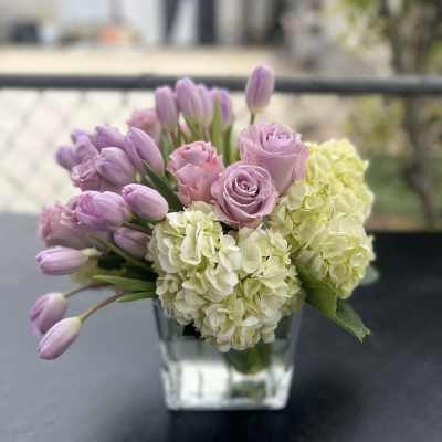 Lavender tulips and roses with pale hydrangeas in a clear glass vase