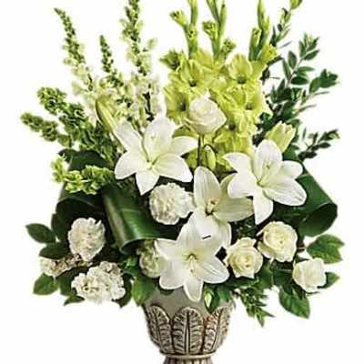 Tall white arrangement of lilies, roses, and carnations in an ornate pedestal vase
