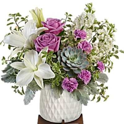 Arrangement of white lilies, lavender roses, purple carnations, stock, and a succulent in a white pot on a wooden stand