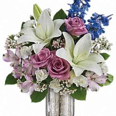 Mixed bouquet of white lilies, lavender roses, and blue flowers in a silver vase